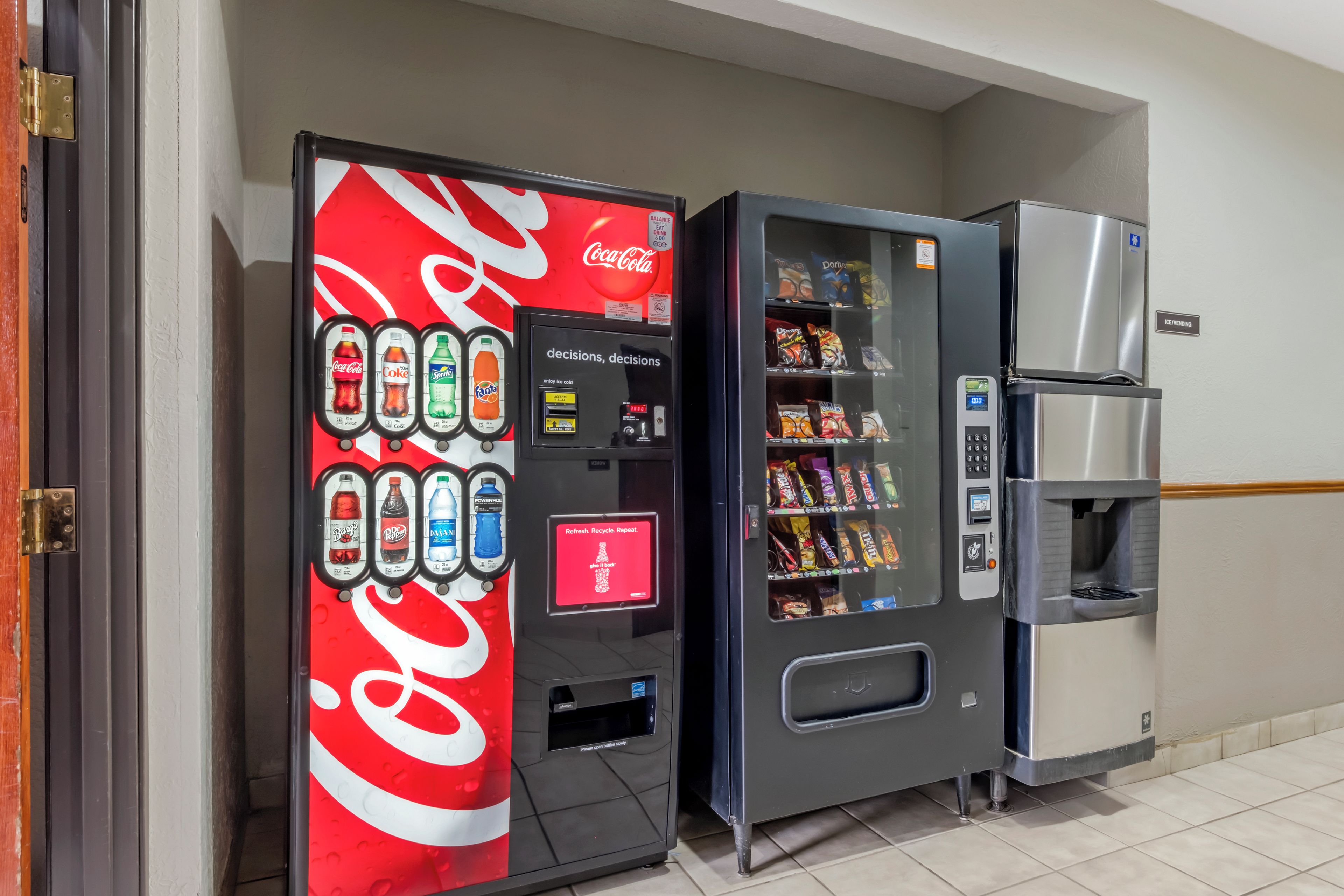 Una máquina expendedora con el logotipo de Coca-Cola y otra máquina expendedora de aperitivos junto a un refrigerador.