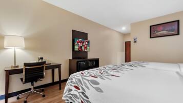 Una habitación de hotel con cama, escritorio, silla, lámpara, televisión y una obra de arte en la pared.