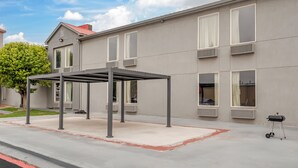 A building with a covered outdoor seating area, multiple windows, and a tree in the background. - Red Roof Inn Dumas (Dumas)