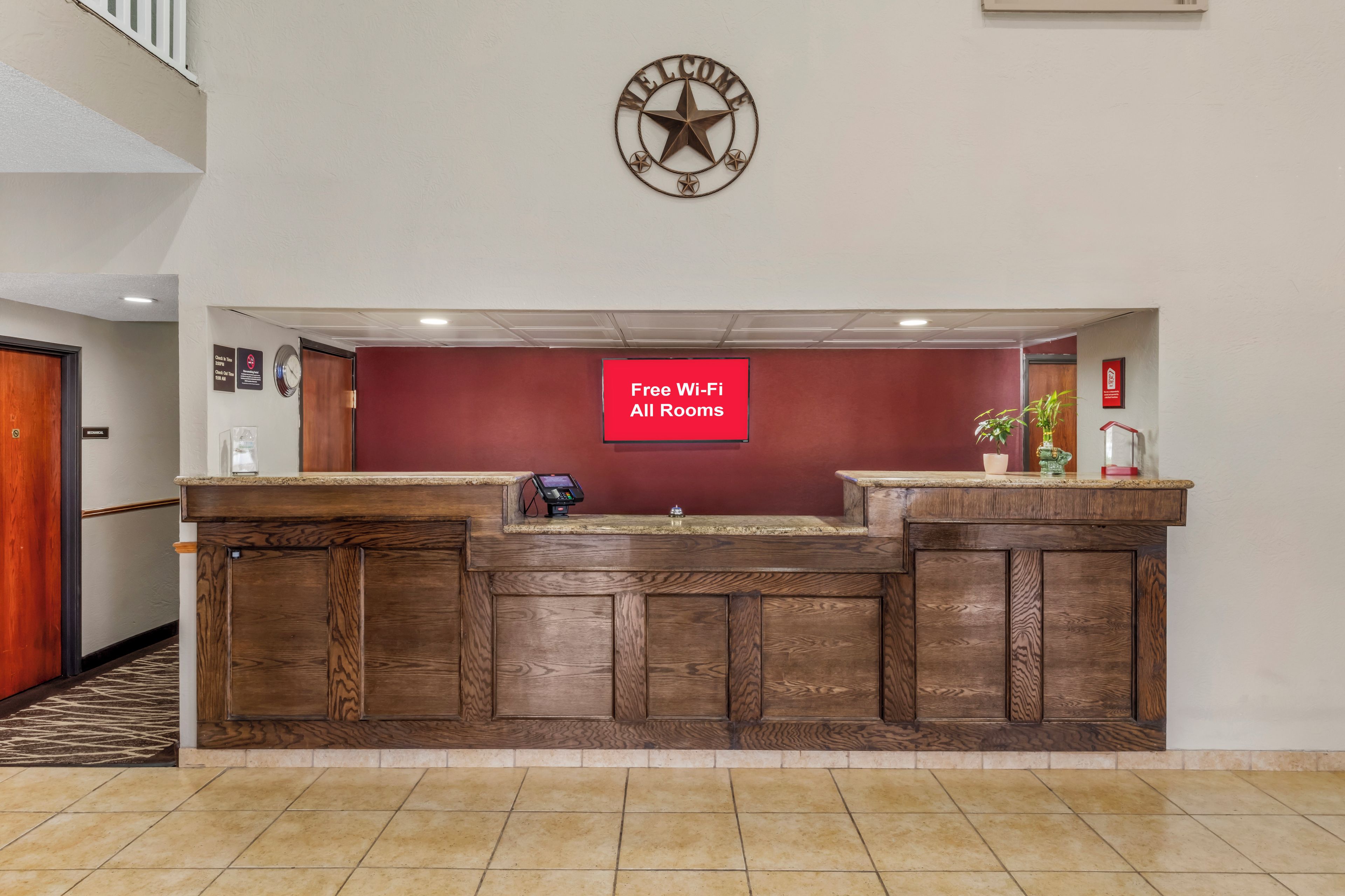 A reception desk with a clock above it, a sign indicating free Wi-Fi, and a red wall.