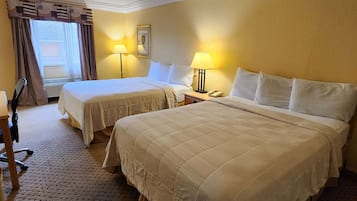 Habitación de hotel con dos camas, un escritorio y una silla. Hay dos lámparas de noche y una ventana con cortinas.