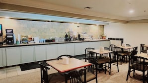 A hotel restaurant with a long counter, multiple tables, and chairs. - Super 8 by Wyndham Temple I-35 (Temple)