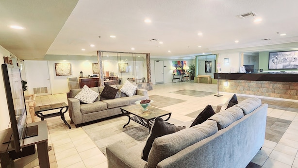 A spacious living area with a sofa set, a coffee table, and a television. There is a reception desk with a computer and a framed picture on the wall. - Super 8 by Wyndham Temple I-35 (Temple)