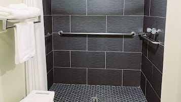 A shower area with dark tiles, a white towel rack, and a small white stool.