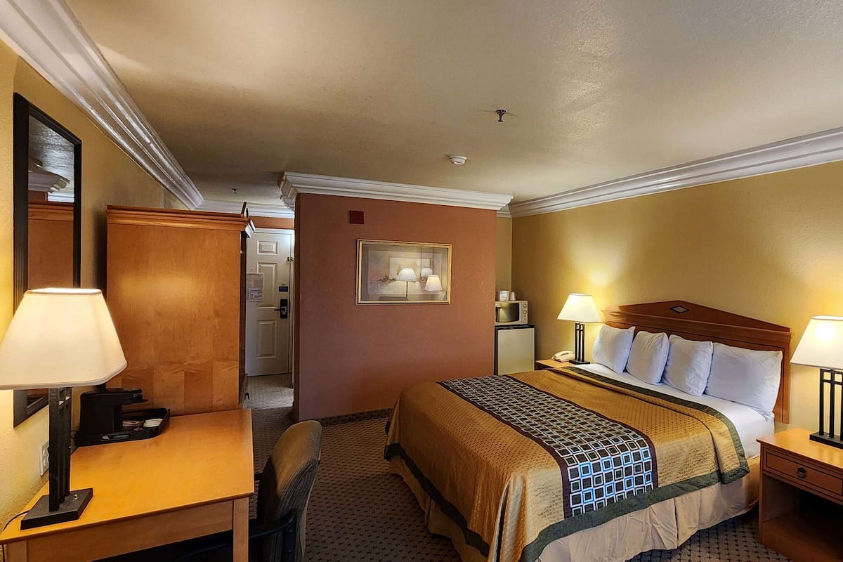 A hotel room with a bed, bedside lamps, a desk with a lamp, a chair, and a small table.