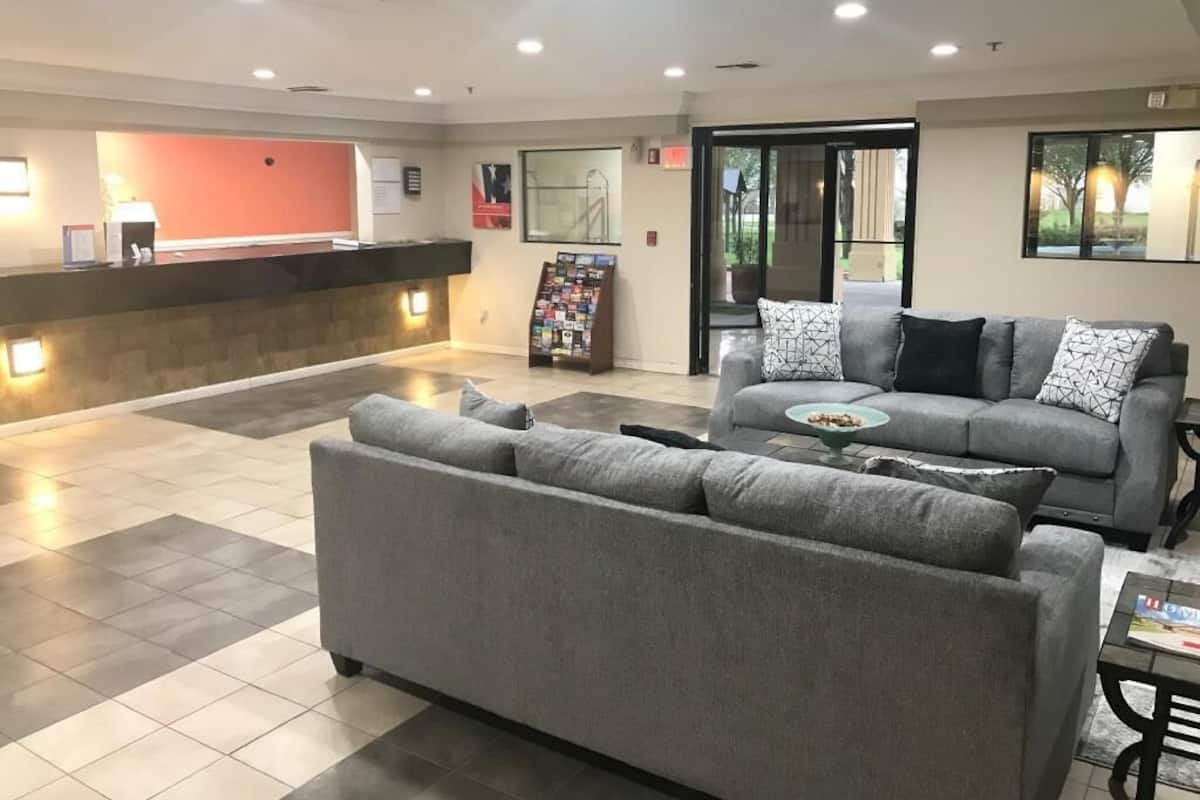 A modern lobby with a reception desk, a grey sofa, a coffee table, and a magazine rack.
