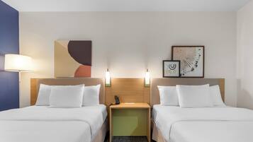 A hotel room with two beds, a nightstand, wall art, and a lamp.