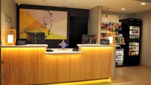 Ein Hotel-Rezeptionsschalter mit modernem Design, darüber ein großes abstraktes Gemälde sowie eine Minibar, gefüllt mit Getränken und Snacks.