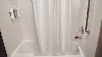 Una bañera blanca con cortina de ducha, un cabezal de ducha manual y un asidero.