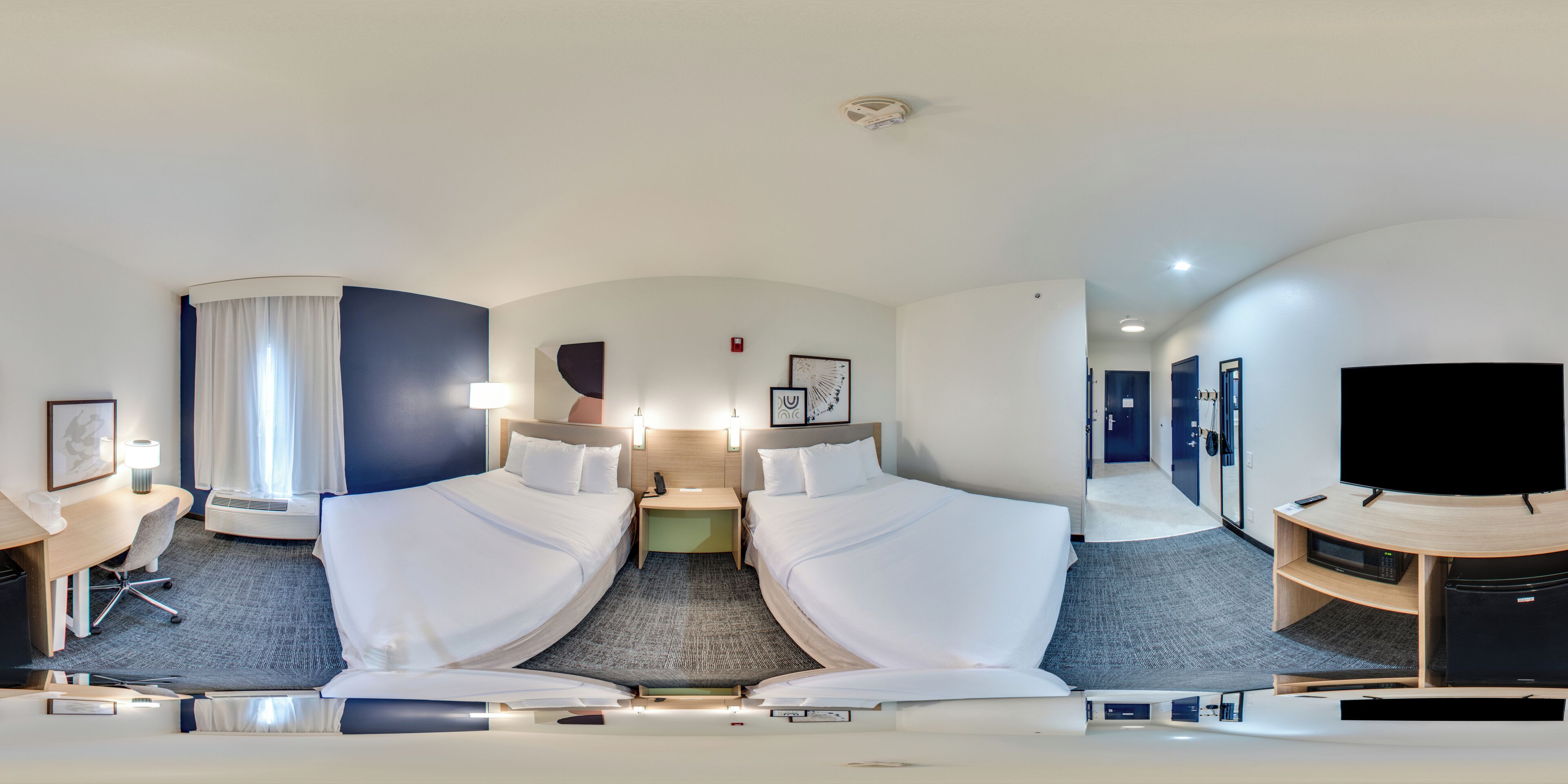 Habitación de hotel con cama, mesitas de noche, escritorio, silla, televisor y espejo.