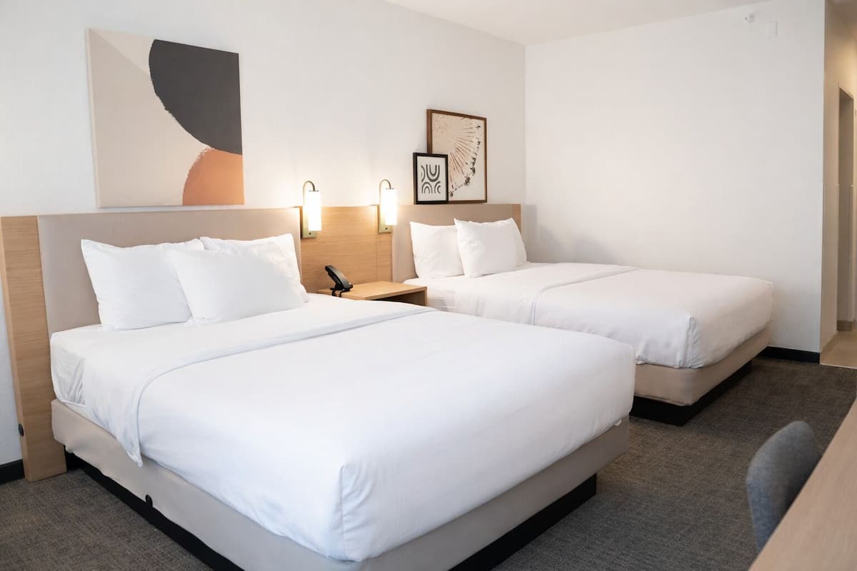 A hotel room with two beds, a desk, a chair, and wall art.