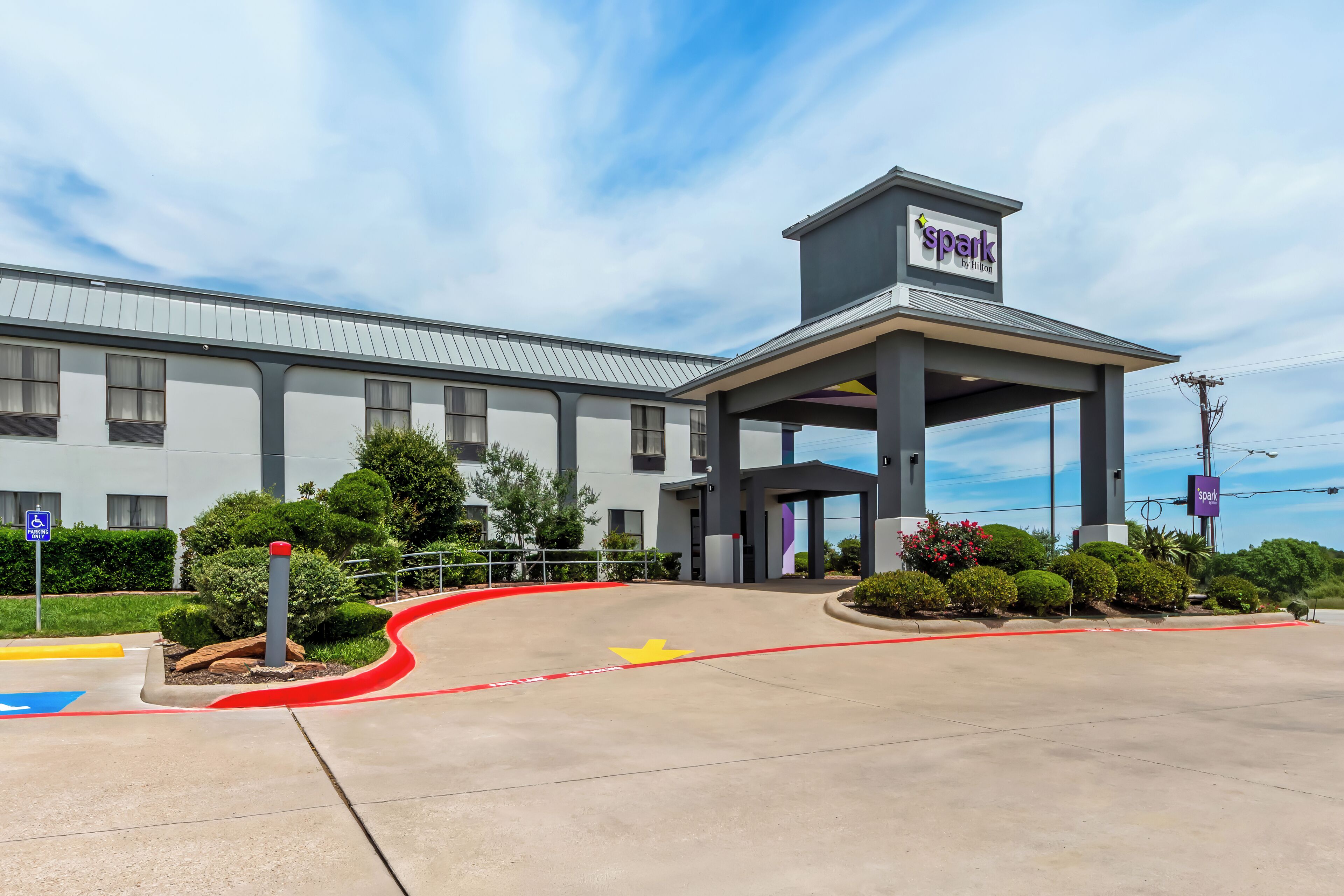 A modern hotel entrance with a covered walkway, a parking lot, and a clear sky.