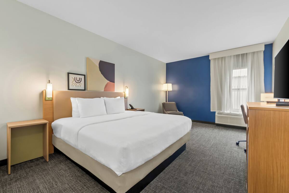 A hotel room with a large bed, bedside tables, a desk, and a television.