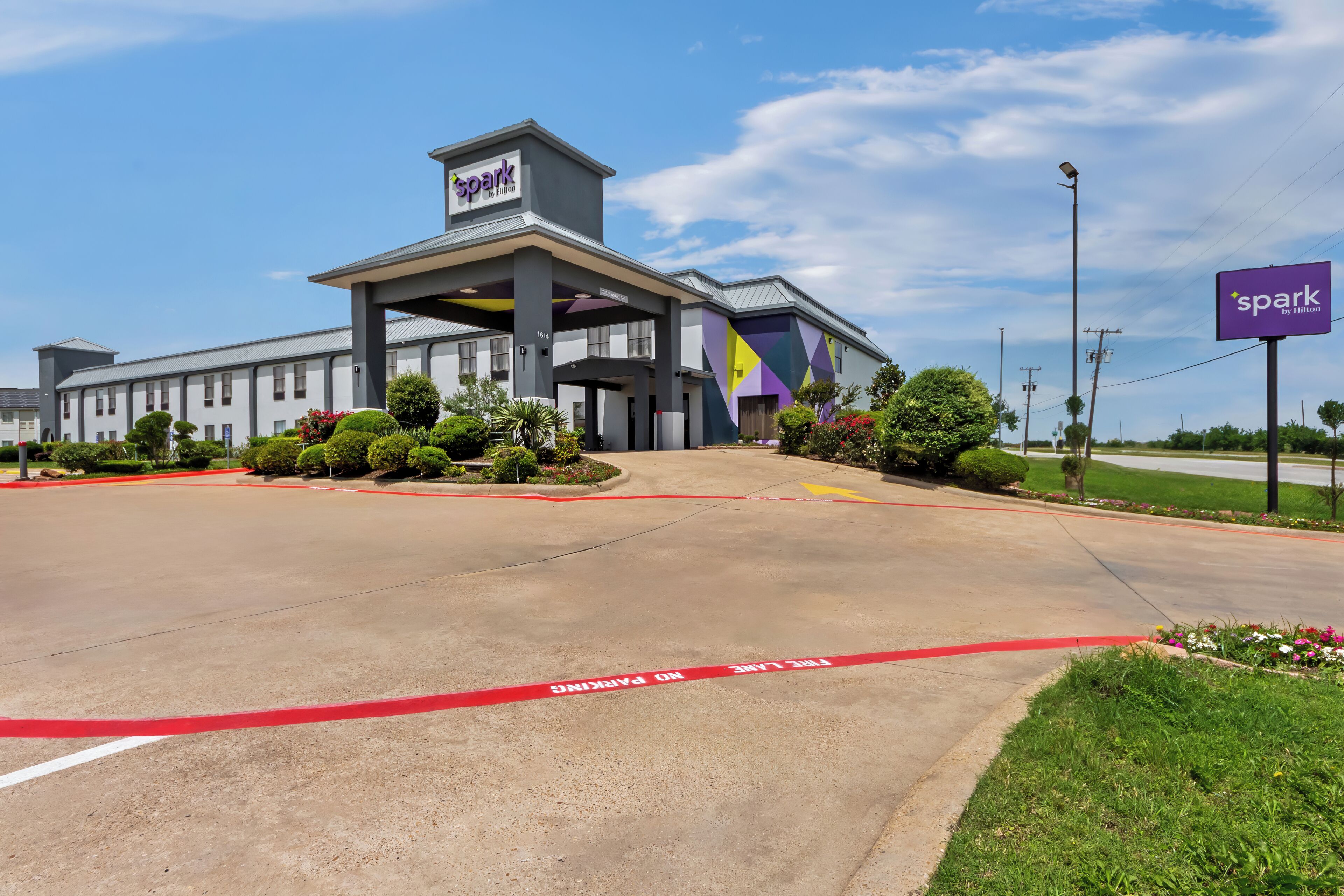 A hotel with a modern design, a covered entrance, and a parking lot with a 'No Parking' sign.