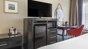A hotel room with a flat-screen TV, a minibar, a desk with a chair, a large mirror, and a window with curtains. - Comfort Inn Plano-Dallas (Plano)