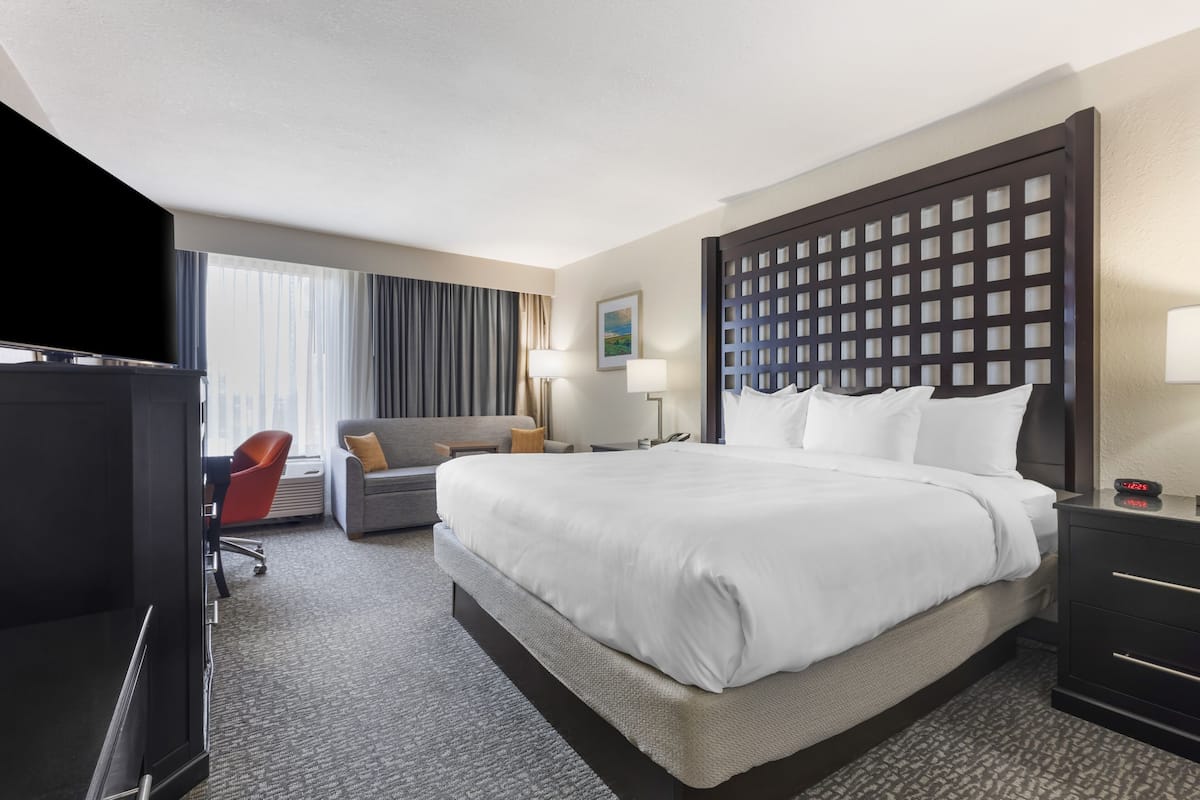Quarto de hotel com uma cama grande, uma escrivaninha com cadeira, televisão e janela com cortinas.