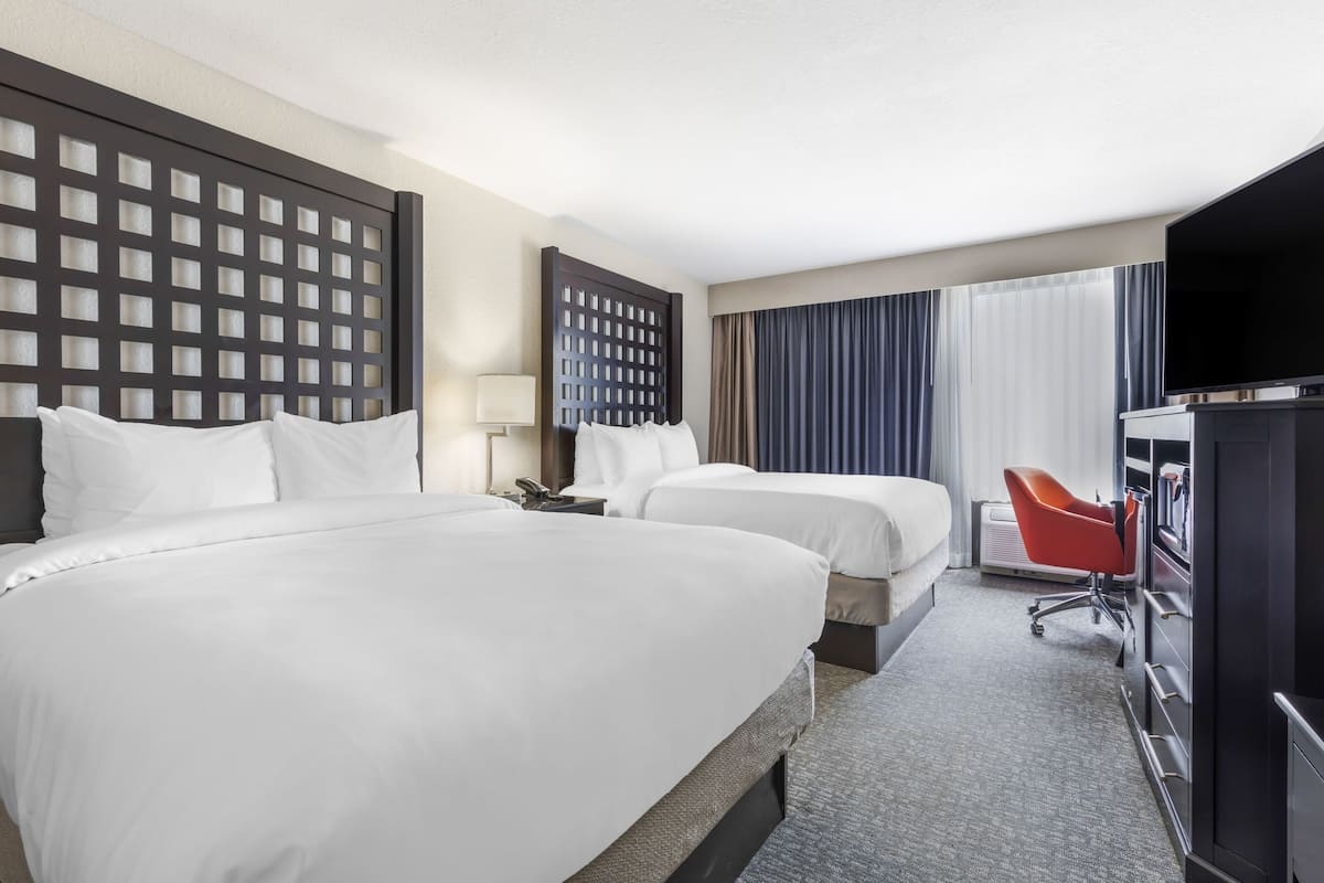 Quarto de hotel com duas camas, televisão, escrivaninha e uma cadeira.