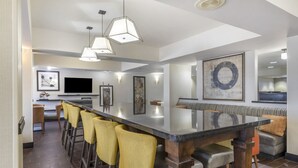 A modern kitchen with a long island, bar stools, pendant lighting, and artwork on the walls. - Comfort Inn Plano-Dallas (Plano)