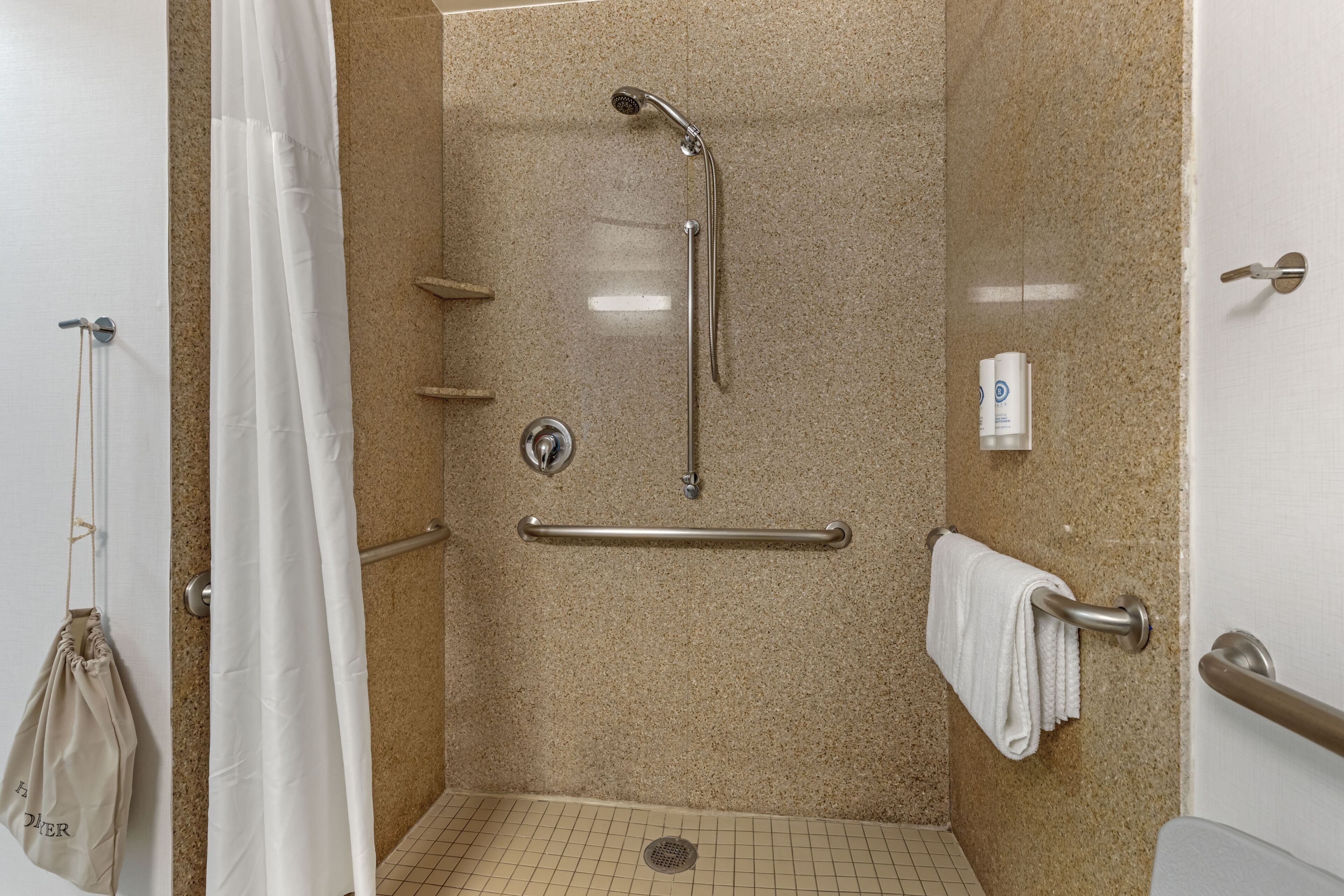 A shower area with a grab bar, a towel rack, and a hand dryer.
