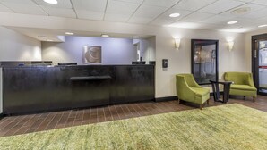 A reception area with a dark reception desk, two green armchairs, a small table, and a green carpet. - Comfort Inn Plano-Dallas (Plano)