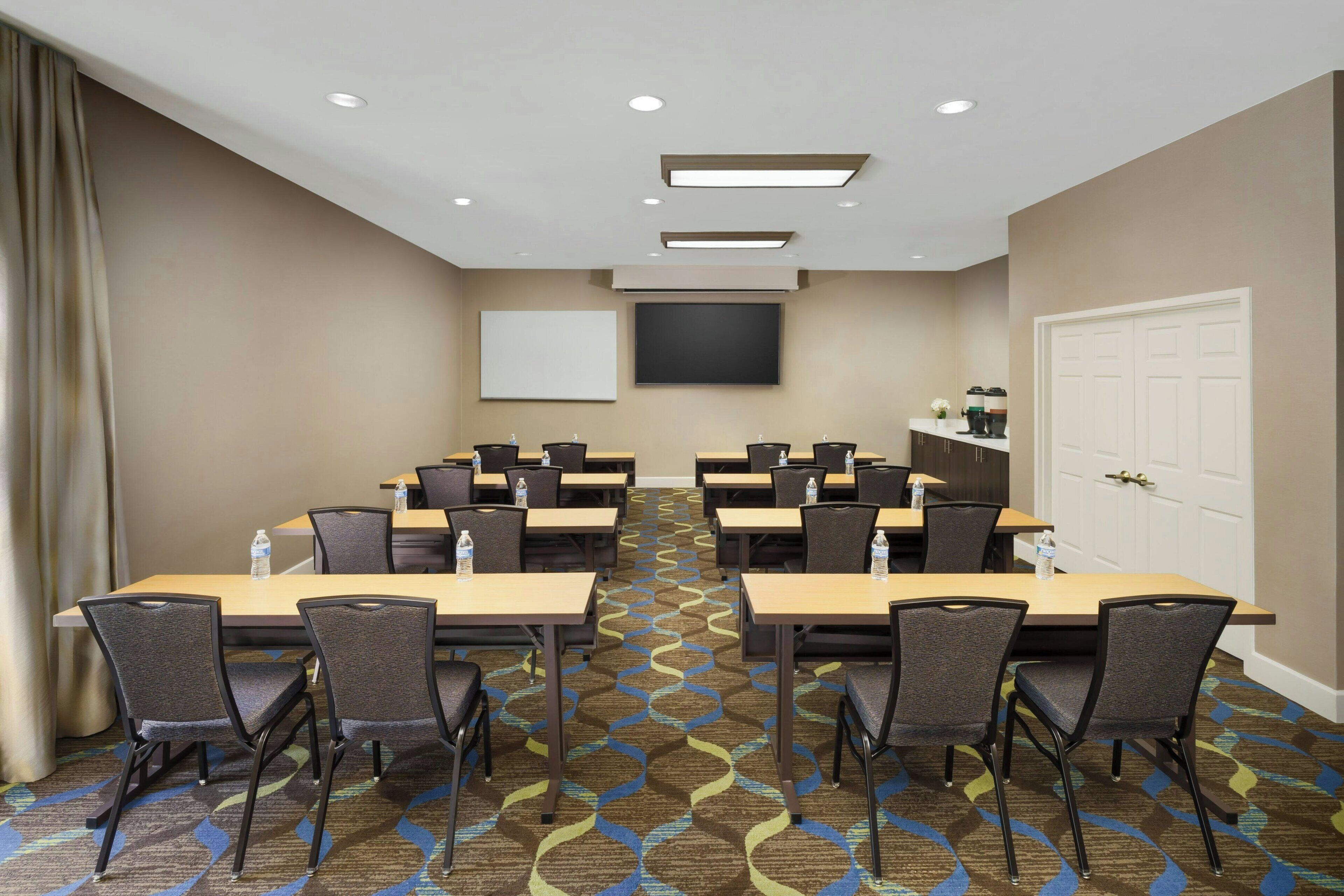 Un salón de conferencias con varias mesas y sillas, una pantalla grande y una puerta.