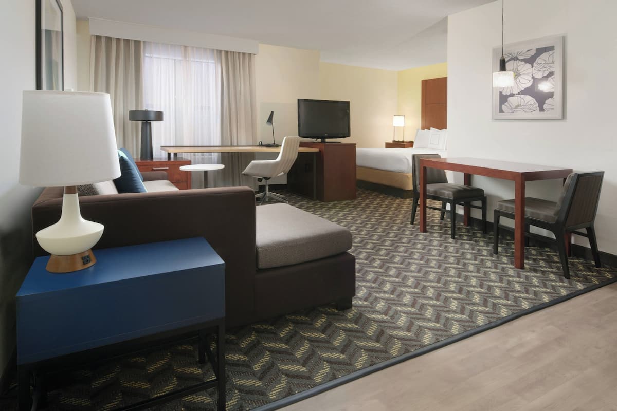 A hotel room with a sofa, a desk, a television, and a bed.