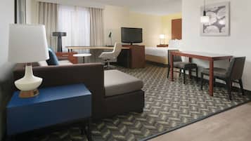 Een hotelkamer met een slaapbank, bureau, televisie en bed.