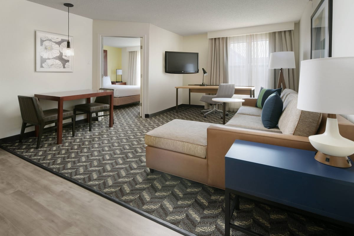 A hotel room with a bed, a desk, a chair, a sofa, a TV, and a lamp.