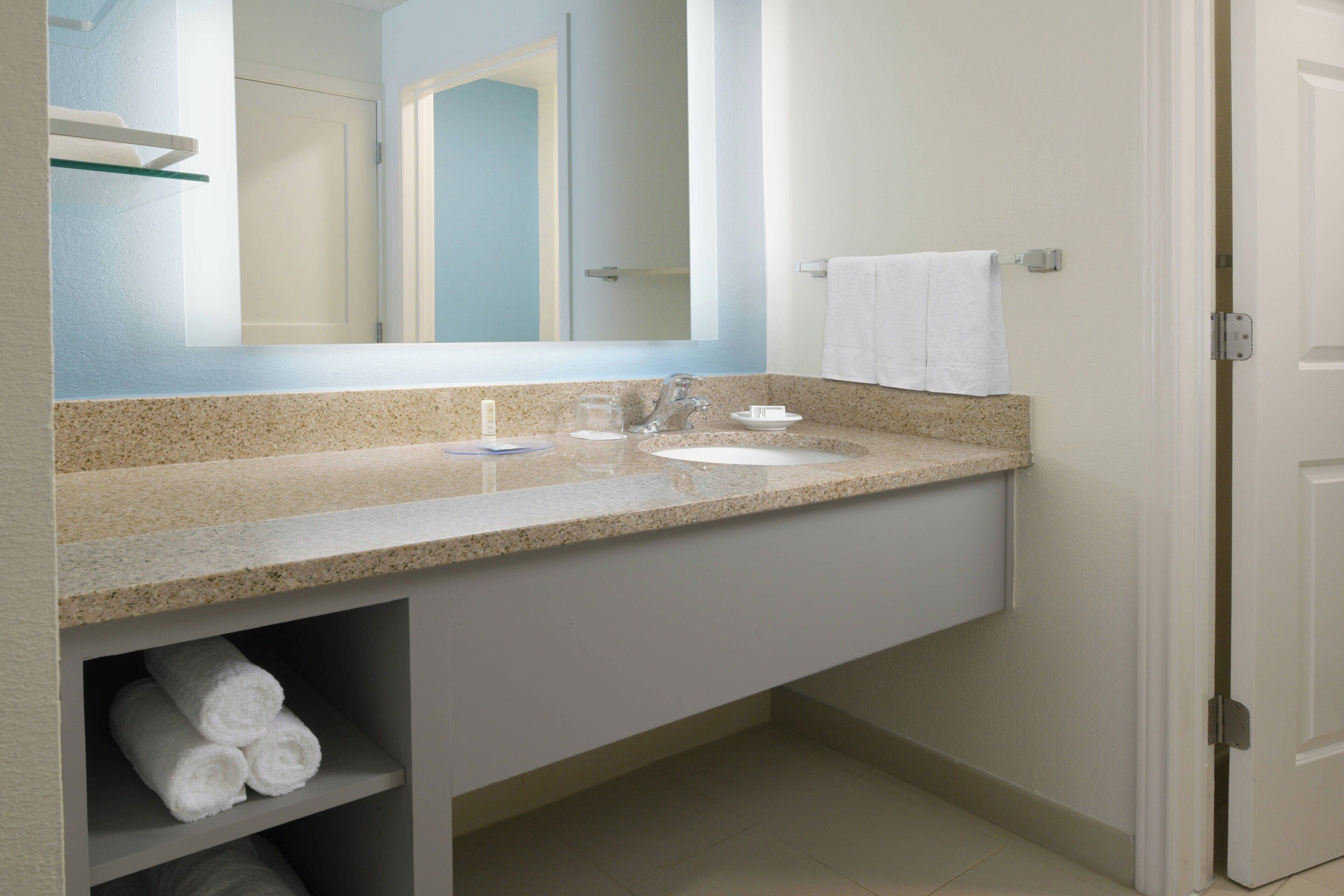 A bathroom with a granite countertop, a sink, a mirror, and a towel rack.