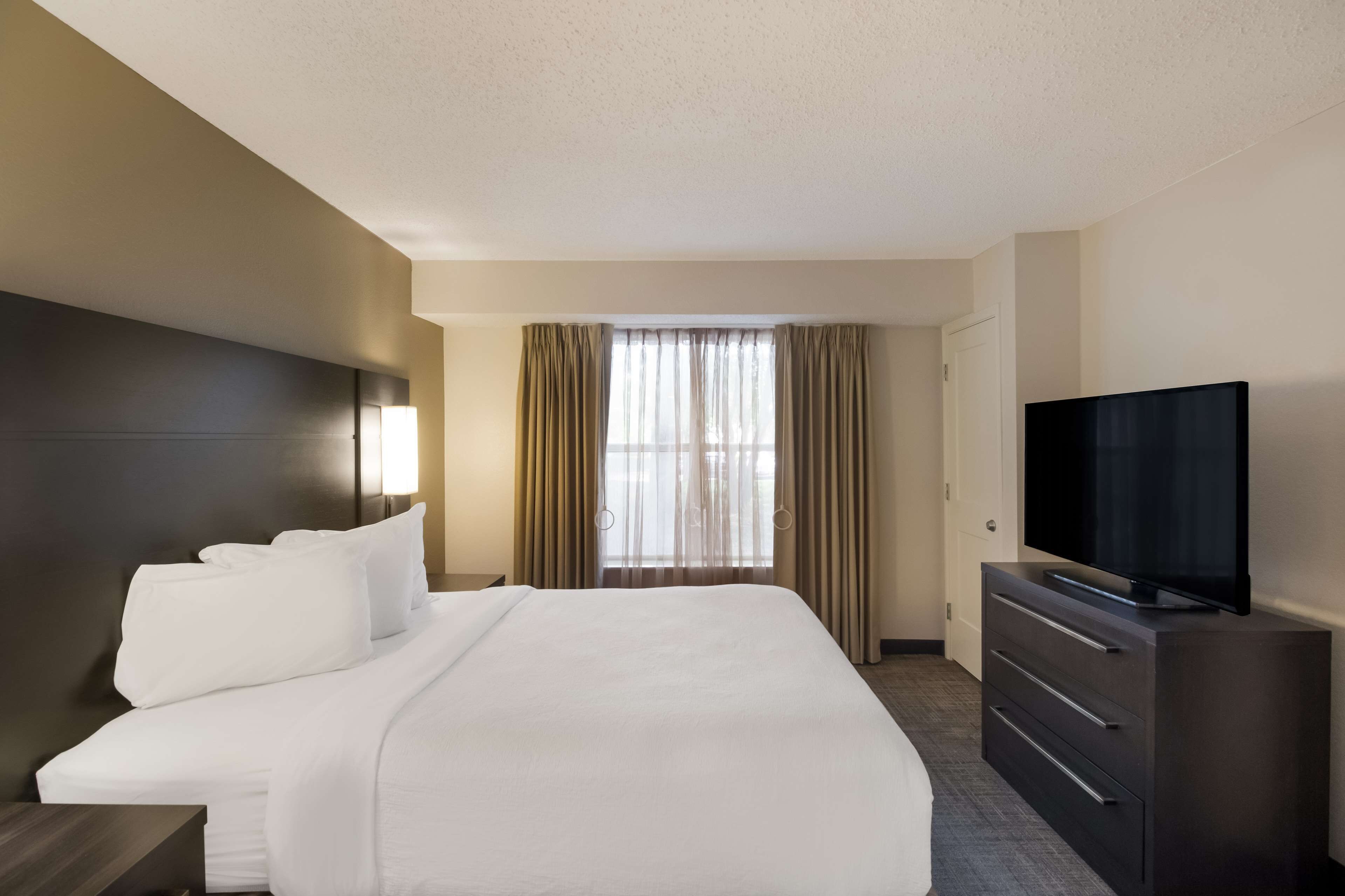 A hotel room with a large bed, a flat-screen TV, a dresser, and a window with curtains.