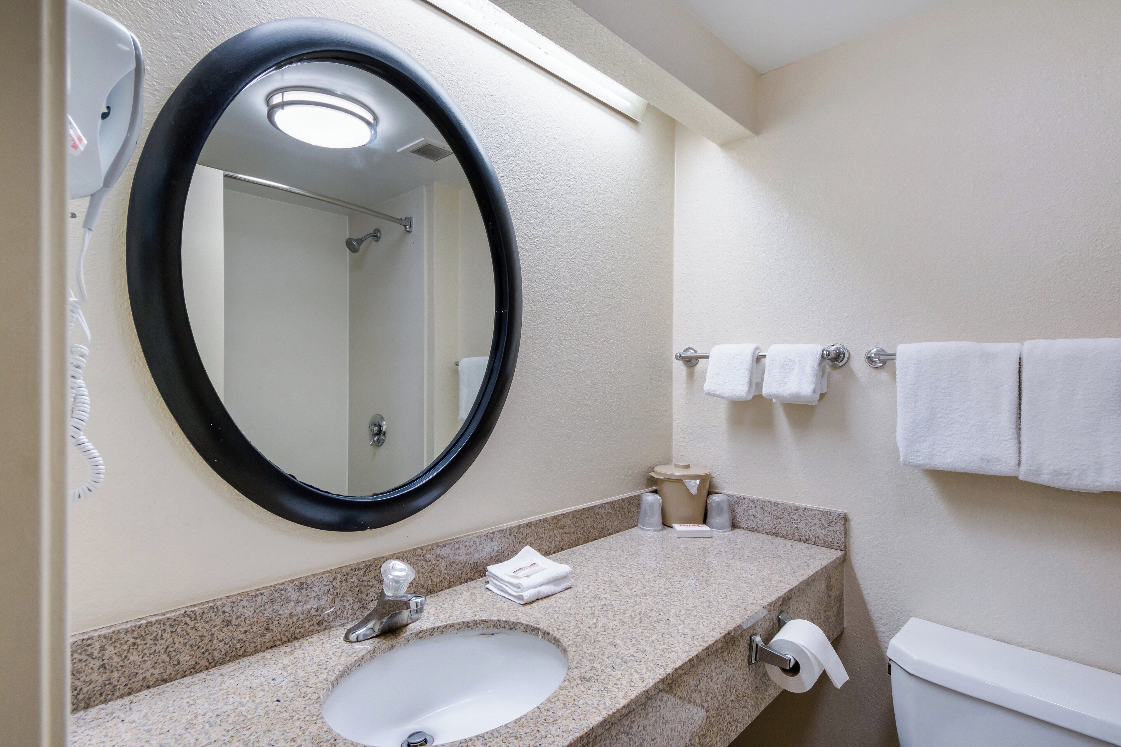 A bathroom with a round mirror, a sink, a toilet, and a towel rack.