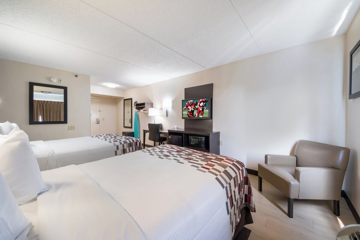 A hotel room with two beds, a desk, a TV, and a chair.