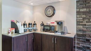 Uma cozinha compacta com cafeteira, micro-ondas e um relógio na parede.