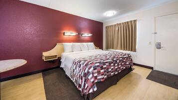A hotel room with a bed, a bedside table, a wall-mounted light, a door, and a window with curtains.