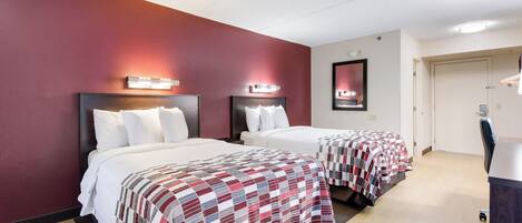 A hotel room with two beds, a red wall, and a door to the right.