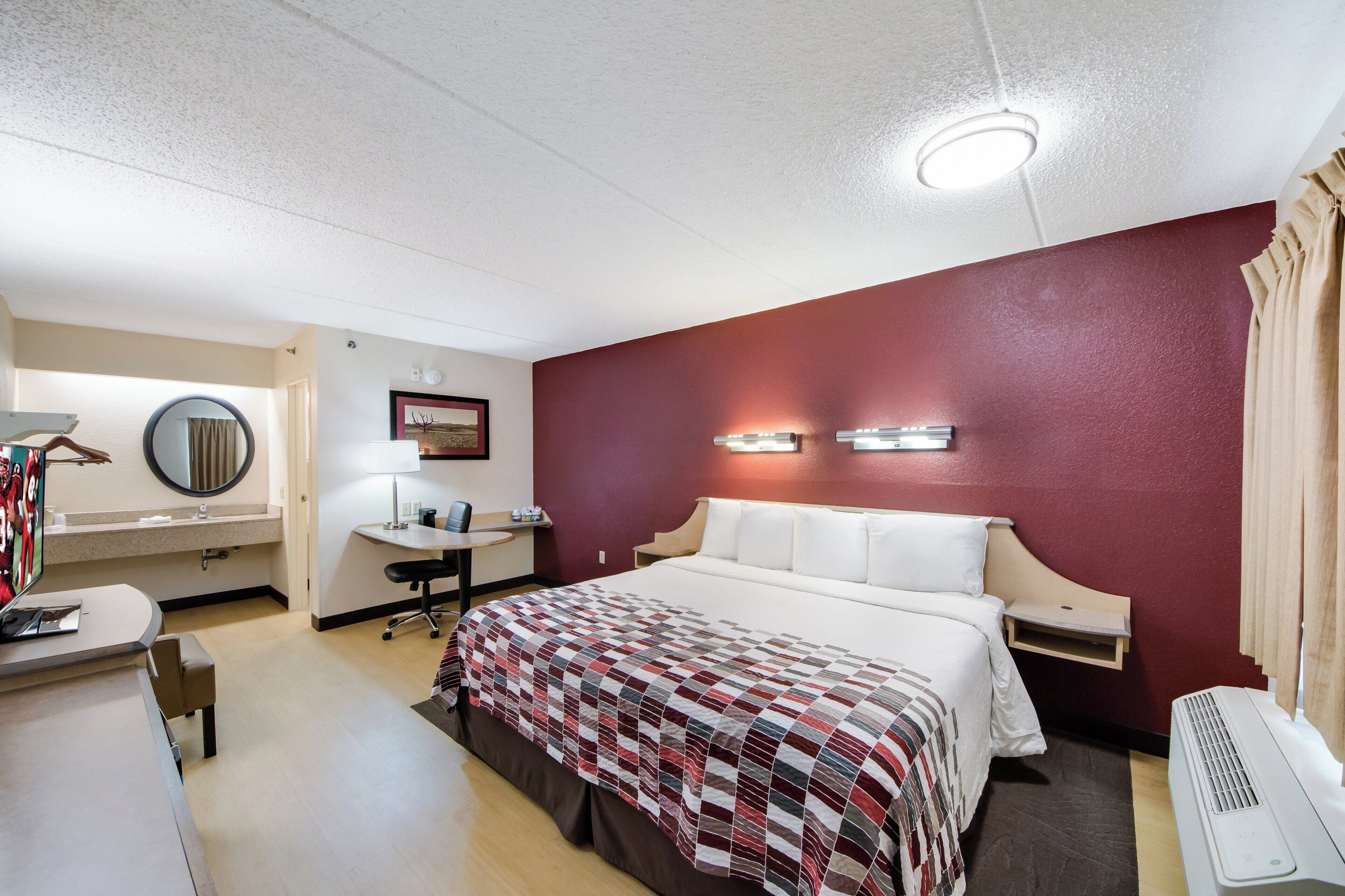 Une chambre d’hôtel équipée d’un lit, d’un bureau, d’une chaise et d’un climatiseur fixé au mur.
