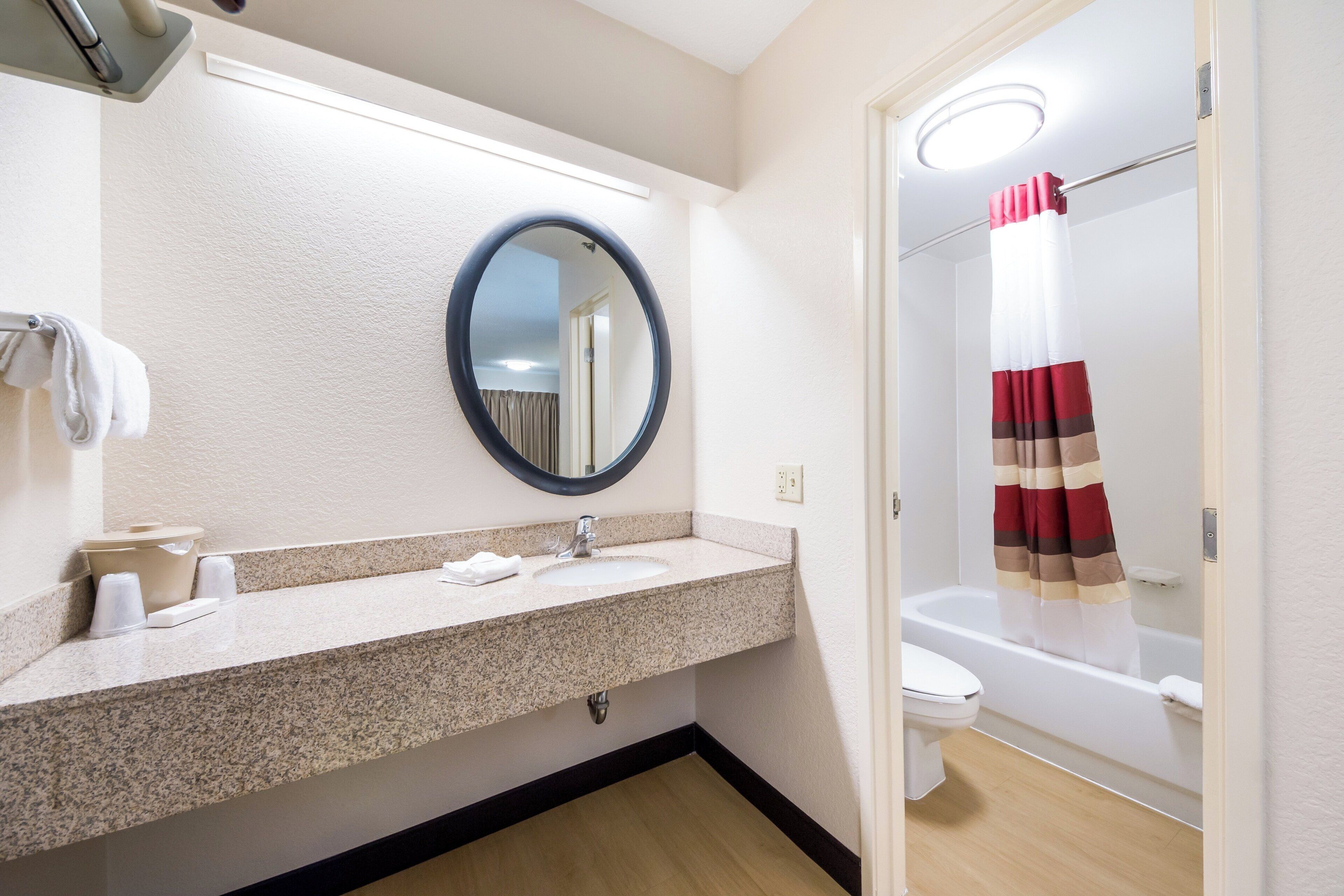 A bathroom with a granite countertop sink, a mirror, a toilet, and a shower area.