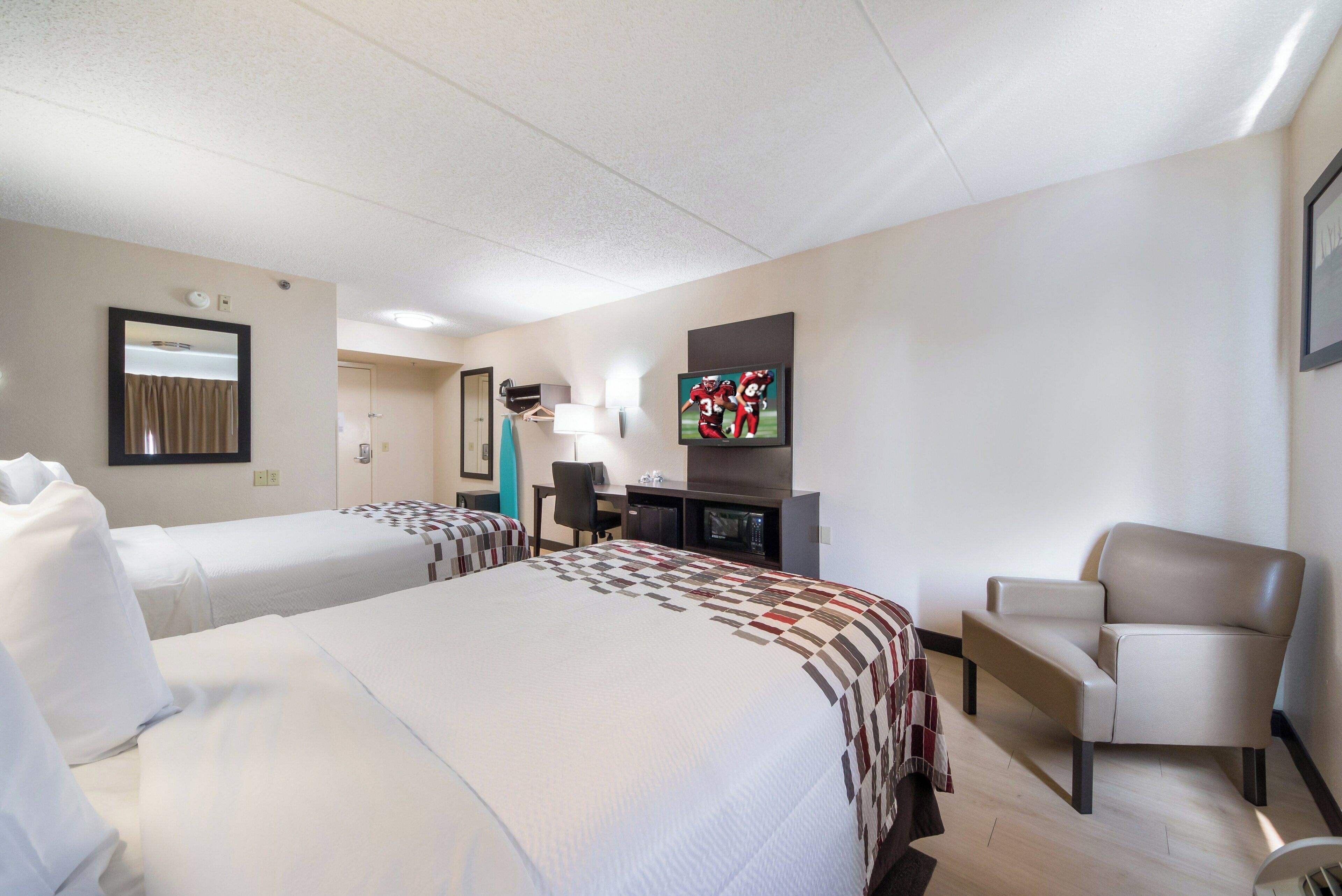 A hotel room with two beds, a desk, a chair, a TV, and a bathroom door.