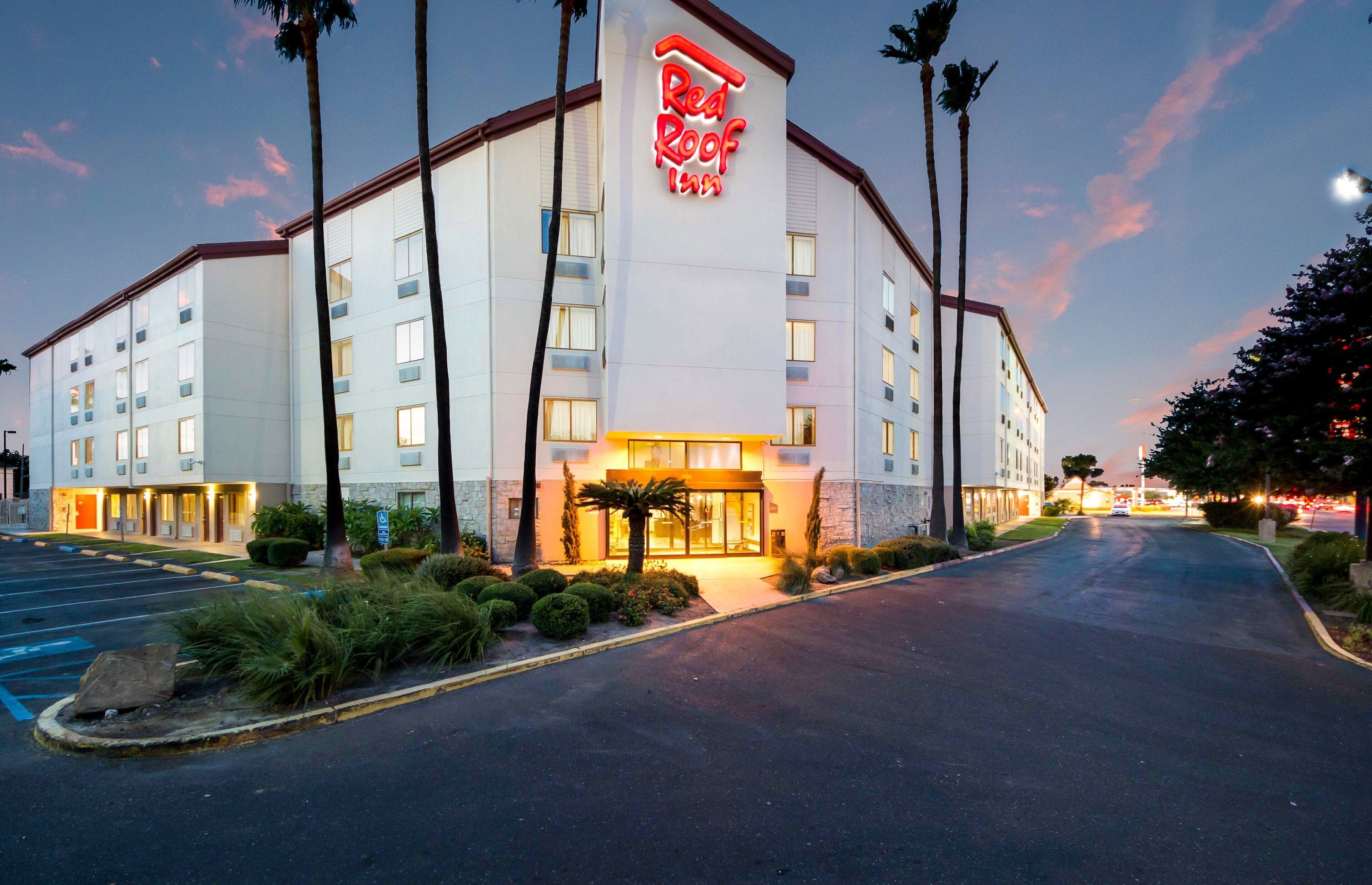 A hotel with a prominent red roof sign, multiple floors, and a parking lot.