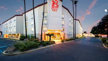 A hotel with a prominent red roof sign, multiple floors, and a parking lot.