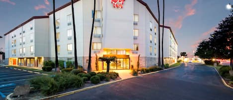 A hotel with a prominent red roof sign, multiple floors, and a parking lot.