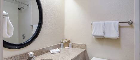 A bathroom with a sink, mirror, towel rack, toilet, and a trash bin.