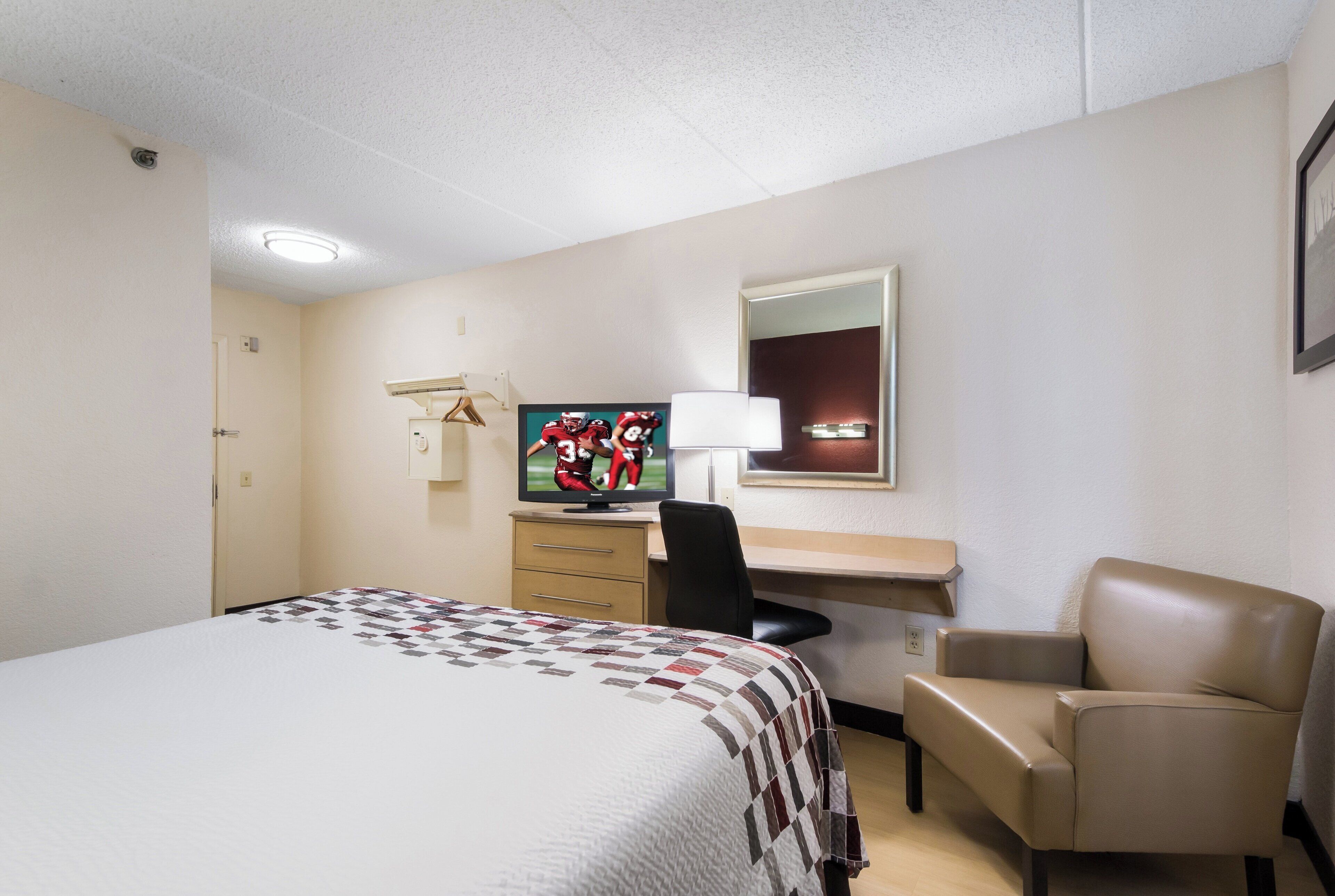 Ein Hotelzimmer mit Bett, Schreibtisch, Sessel, Fernseher und Spiegel.