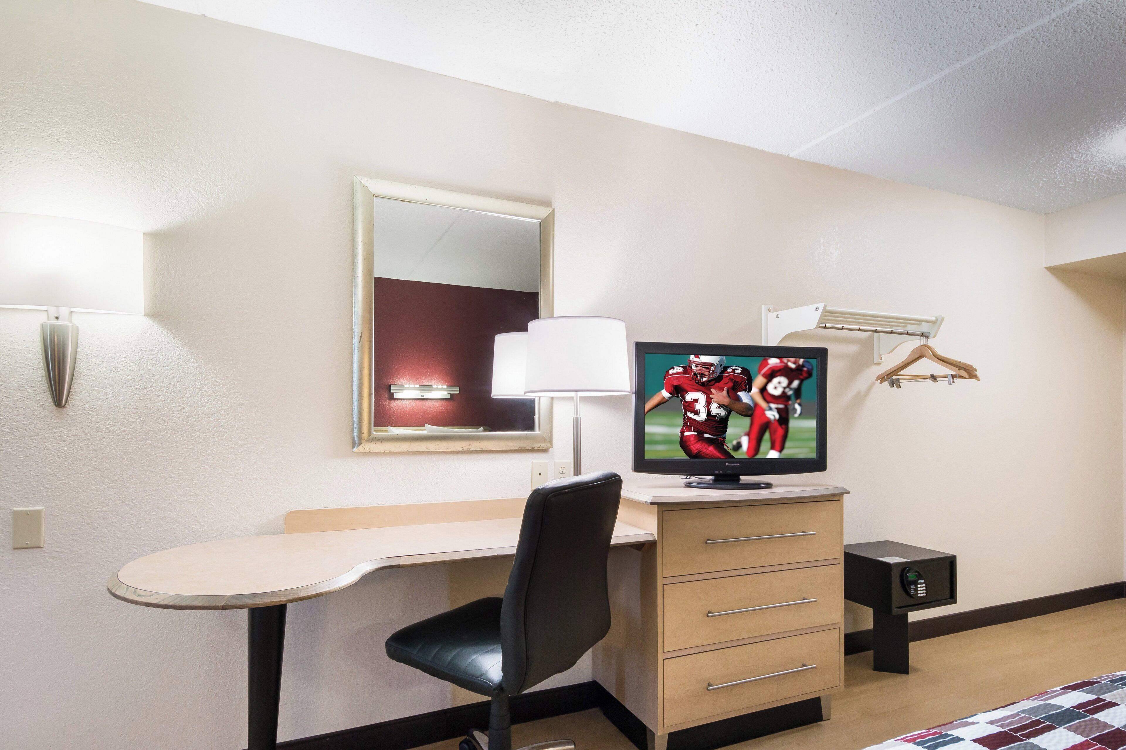 Habitación de hotel con escritorio, silla, televisor y cama con colcha.