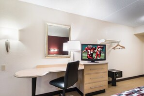 Een hotelkamer met een bureau, stoel, televisie en een bed met quilt.
