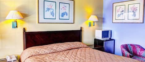 A hotel room with a large bed, two wall-mounted lamps, a television on a stand, and two framed floral artworks on the wall.