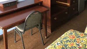 Habitación de hotel con un escritorio de madera, un televisor encima de un aparador, una silla y una cama con colcha estampada.