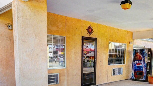 A building with a yellow exterior, a black door, and windows with metal bars. There is a large planter in front and a Pepsi vending machine to the right. - Nites Inn (Killeen)