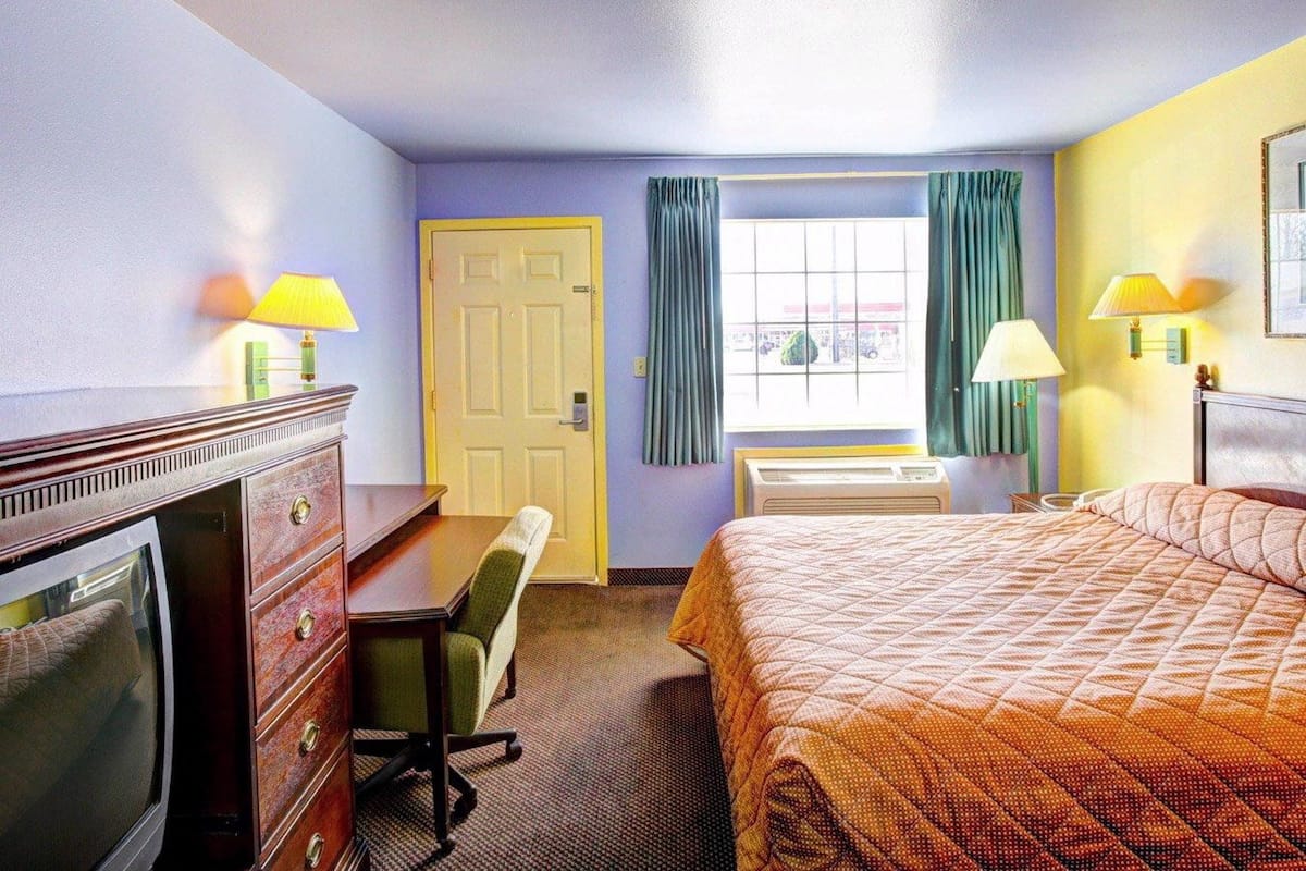 A hotel room with a bed, a desk, a chair, a television, and a window with curtains.