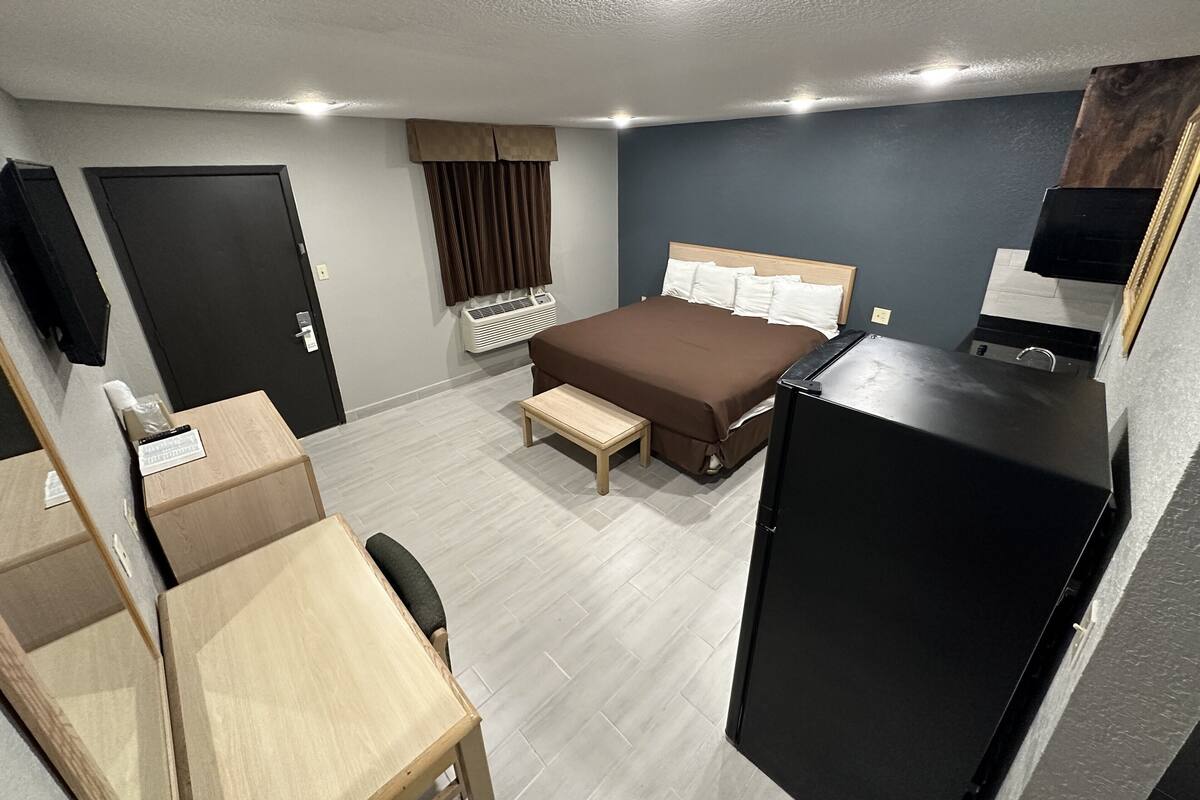A hotel room with a bed, desk, chair, and a small kitchenette.
